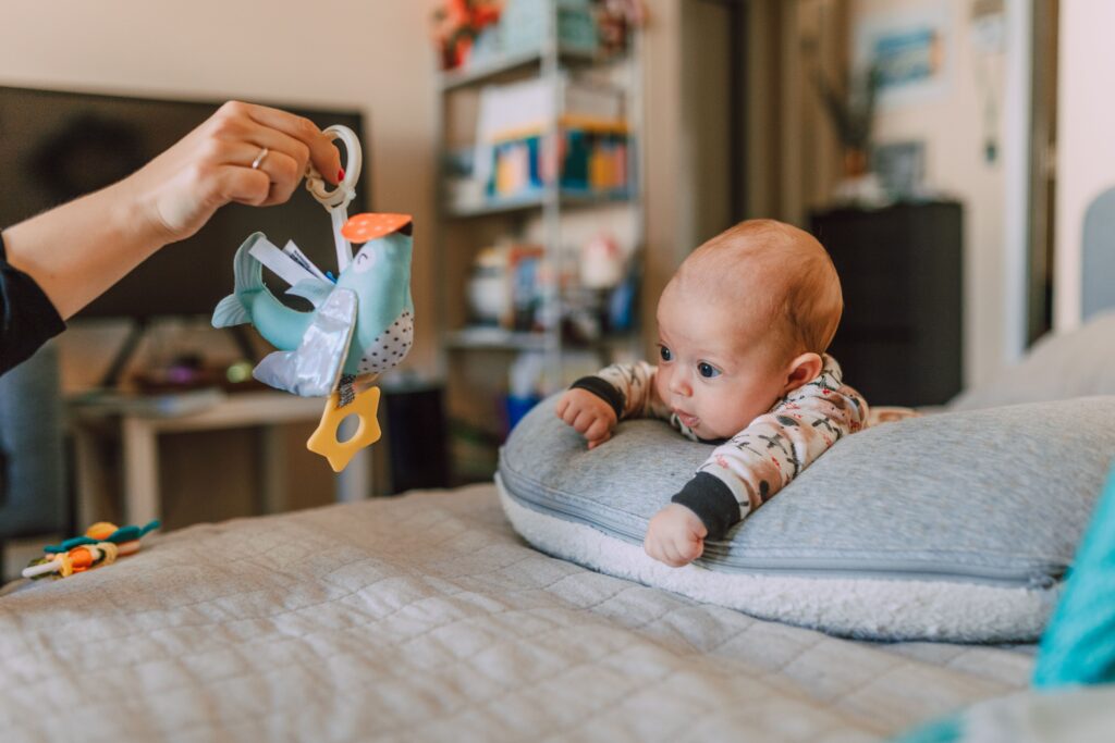 "Best Toys for Babies Who Aren't Crawling Yet" Cute baby showing curiosity while playing with a colorful bird toy in a cozy indoor setting.